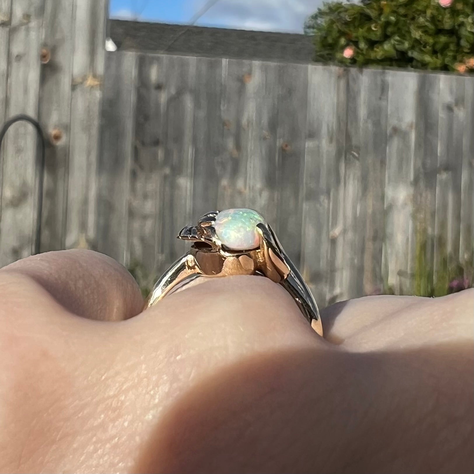 The gallery view of a vintage gold opal ring, worn on a hand in cloudy daylight.