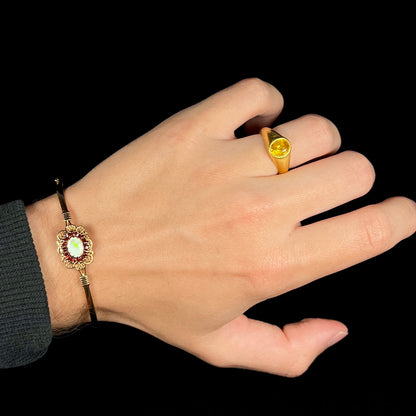 A vintage yellow gold opal and garnet bangle bracelet worn on a wrist, held against a black background.