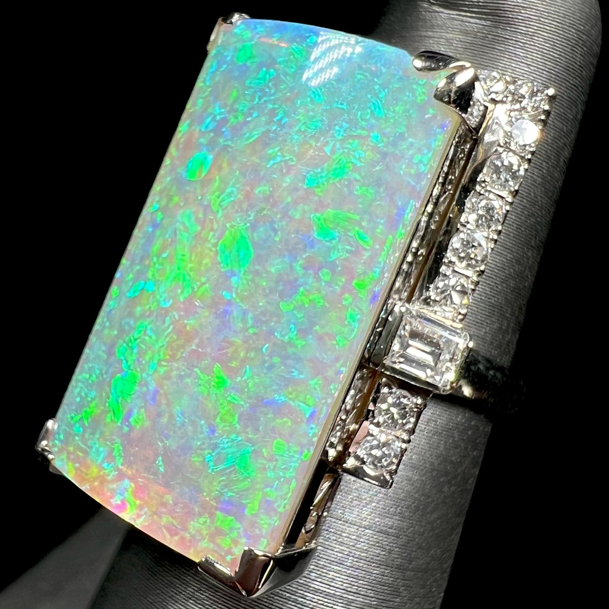 Angled close-up of a vintage Mid-Century era opal and diamond cocktail ring in Japanese platinum, shown on ring display under studio LED light.