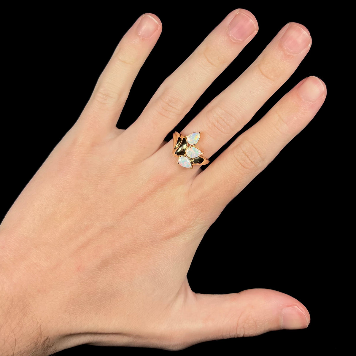 Hand wearing a women's vintage, Modernist-style 14k gold opal ring.  The ring is set with three pear shaped Australian crystal opals.