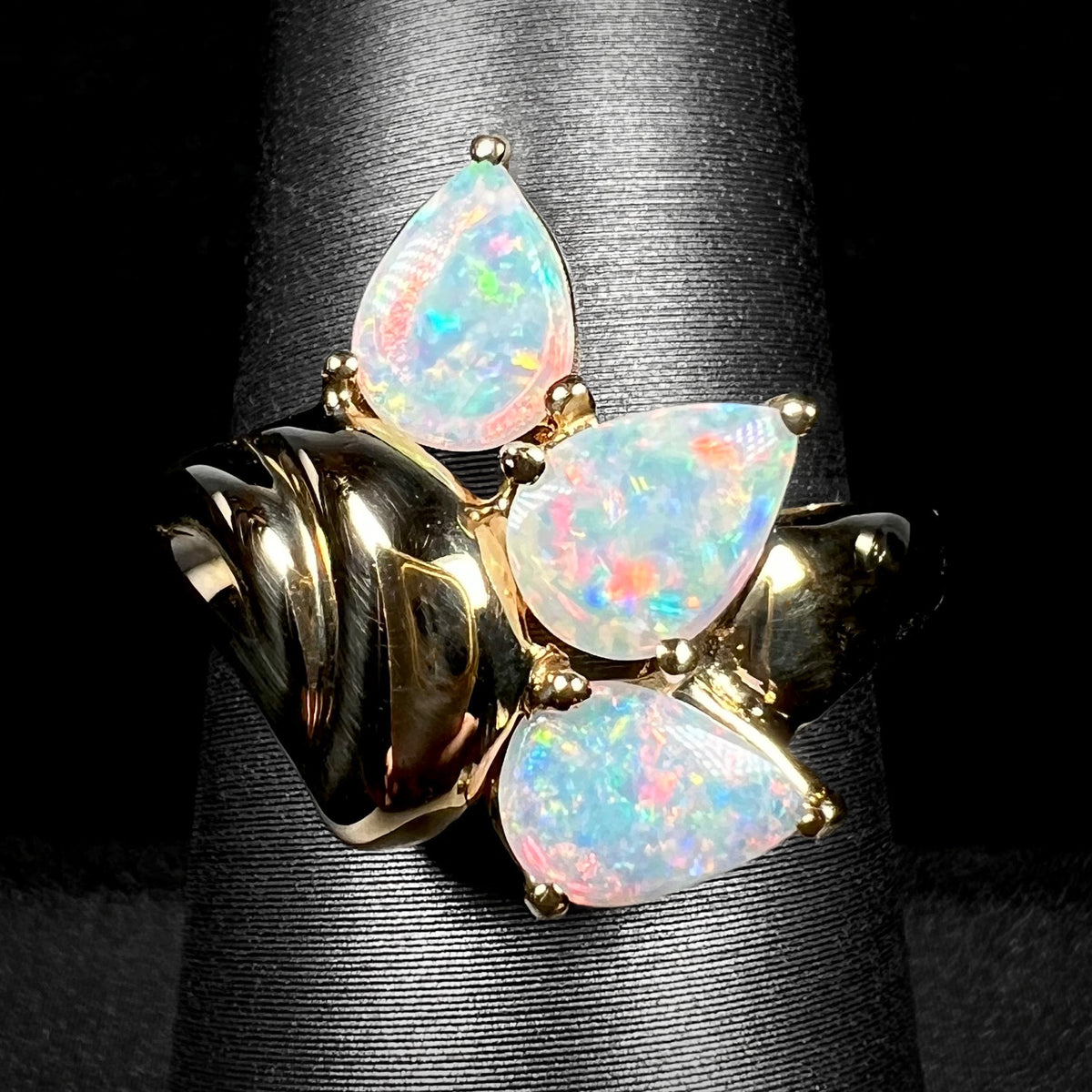 A vintage, Modernist-style three-stone Australian crystal opal ring cast from 14k yellow gold, shown close-up from the front on a ring display.