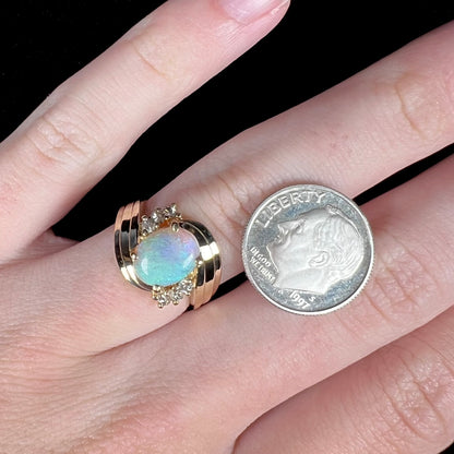 Hand wearing vintage, Modernist style 14k gold crystal opal and six-stone diamond ring next to US dime coin