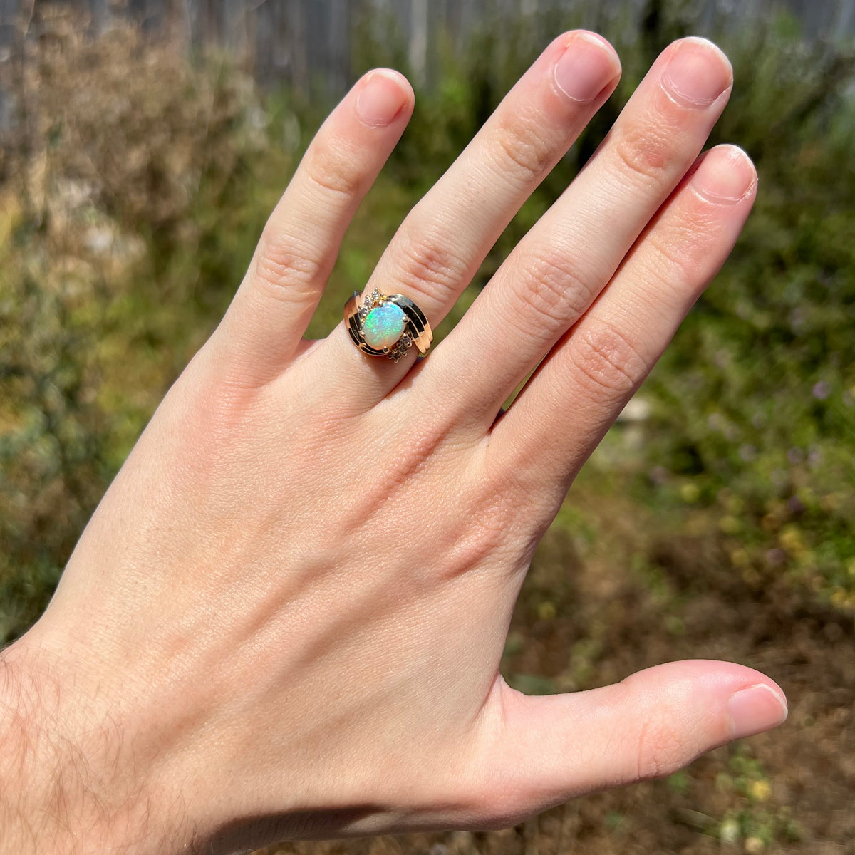 Hand wearing vintage opal and diamond women's ring in 14k gold with Modernist bypass design under natural sunlight