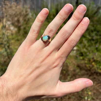 Hand wearing vintage opal and diamond women's ring in 14k gold with Modernist bypass design under natural sunlight