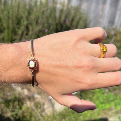 A vintage yellow gold Australian opal and garnet halo bangle bracelet worn on a wrist and shown in sunlight.