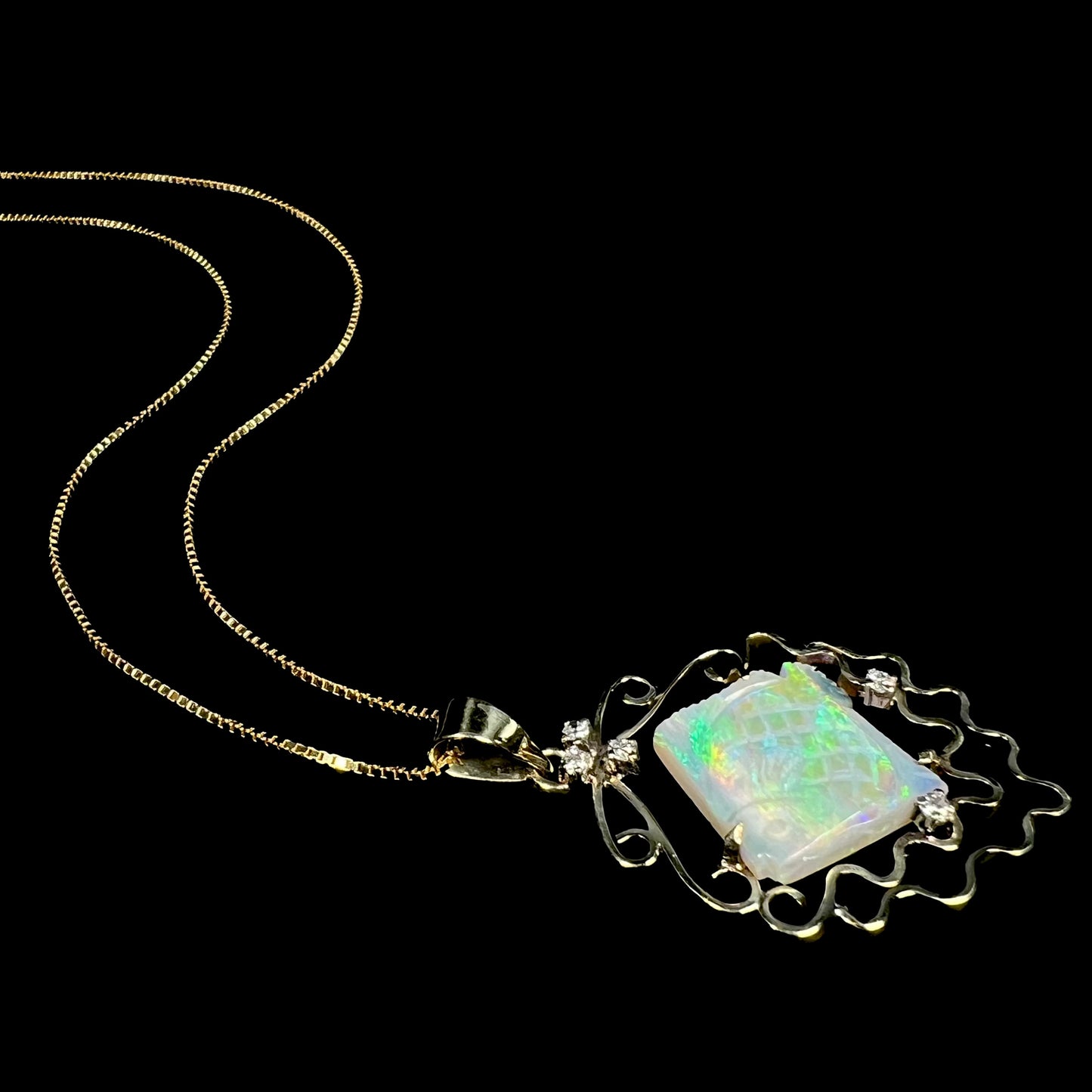 Vintage 1980s era carved opal fish and diamond necklace in 14k gold, laying on black background with chain