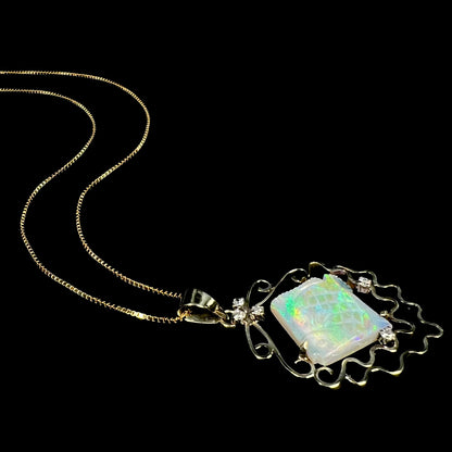Vintage 1980s era carved opal fish and diamond necklace in 14k gold, laying on black background with chain