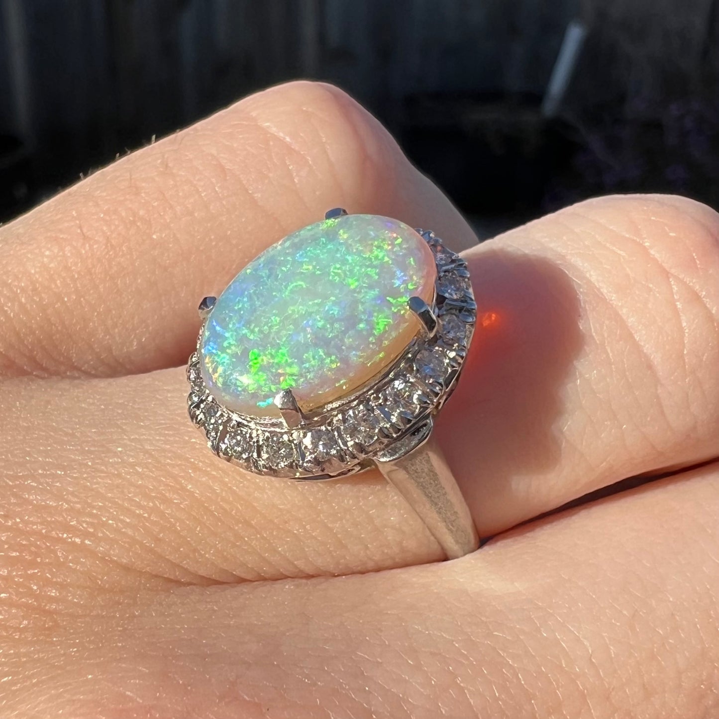 A vintage opal and diamond halo enggagement ring on a hand in the sunlight.