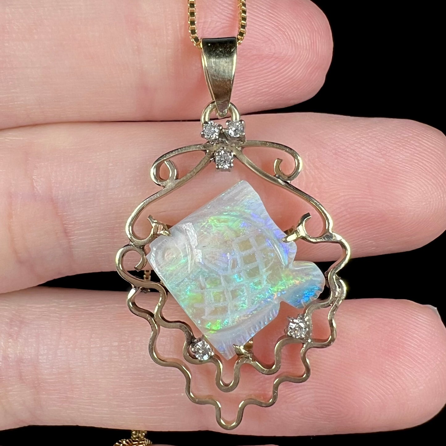 Close-up of vintage 1980s-era carved Australian opal fish pendant with diamond accents representing bubbles, held in hand