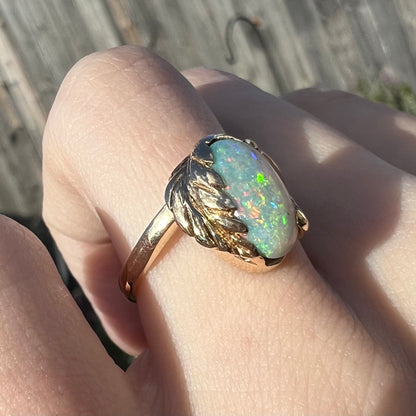 A vintage opal leaf ring set in yellow gold, worn on a finger in the sunlight.