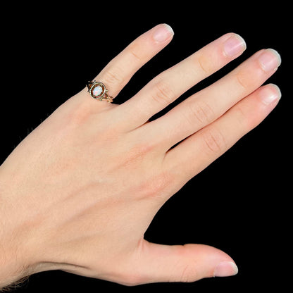 A ladies' Art Nouveau style opal solitaire ring.  The mounting is yellow gold with filigree accents.