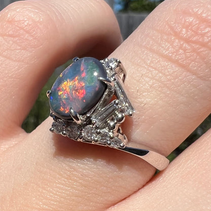 Baguette cut and round cut diamonds in view on shoulder of vintage platinum opal ring, worn on finger and viewed close-up in sunlight.