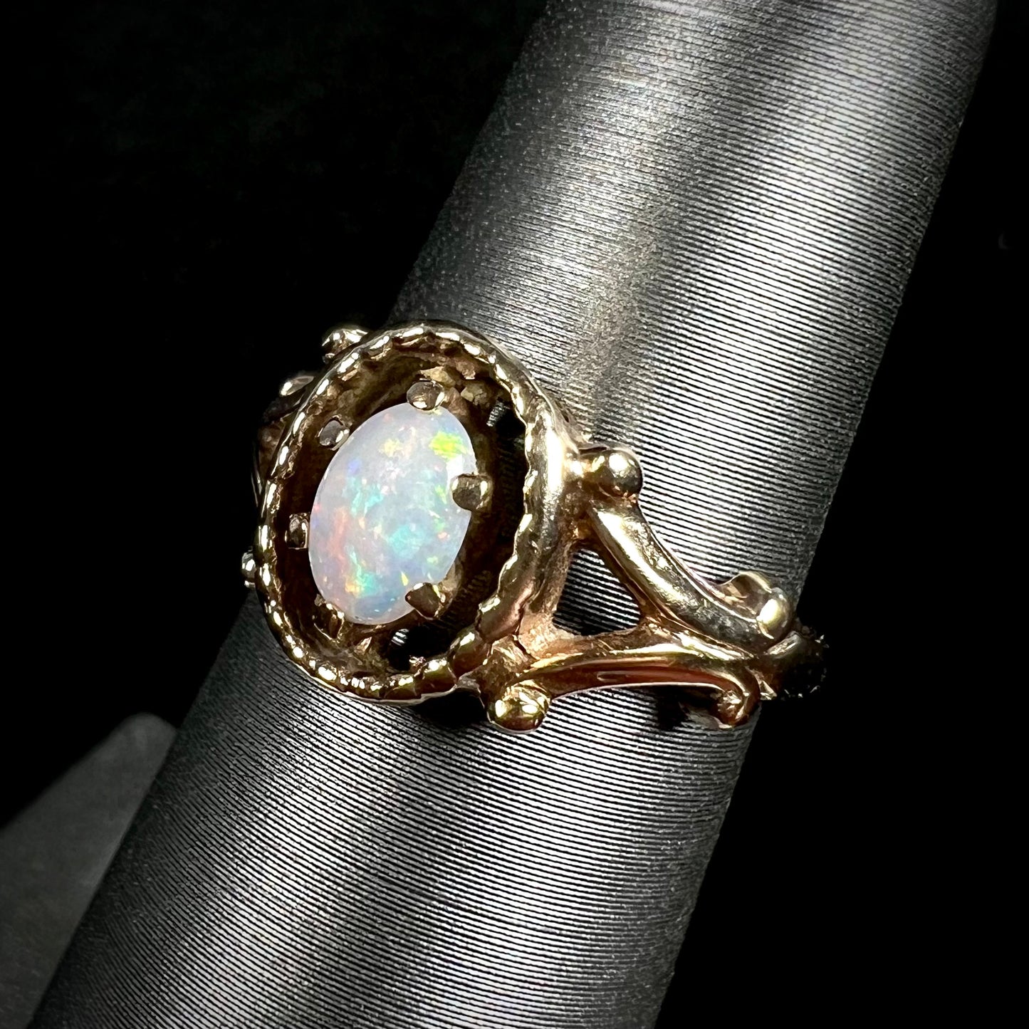 A ladies' Art Nouveau style opal solitaire ring.  The mounting is yellow gold with filigree accents.