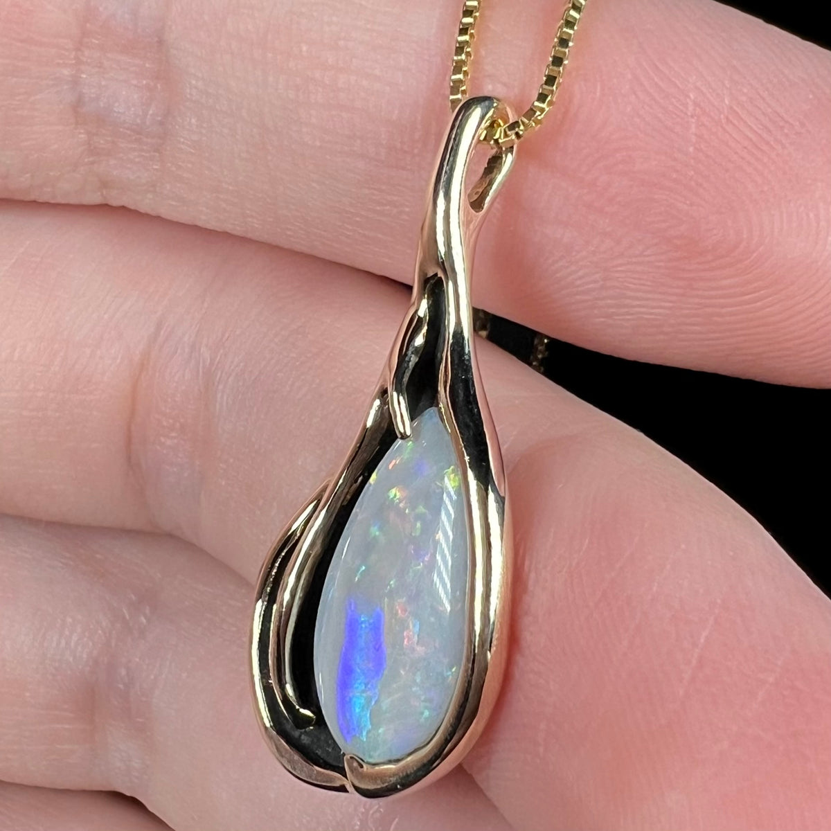 Vintage pear shaped Australian opal pendant in 14k gold shown close-up from angle in hand