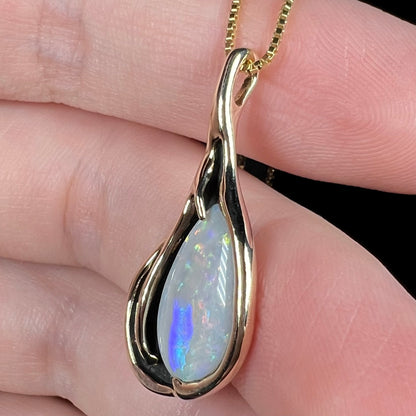 Vintage pear shaped Australian opal pendant in 14k gold shown close-up from angle in hand
