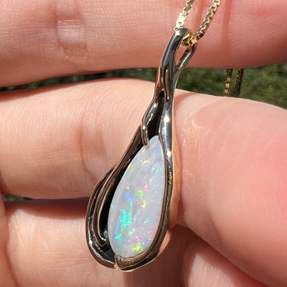 Angled close-up of vintage c.1980s pear shaped Australian opal pendant in gold, held in hand under natural sunlight