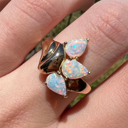 Close-up of vintage, Modernist-style 14k gold ring mounted with three pink Coober Pedy opals, worn on finger in natural sunlight.
