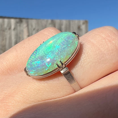 A vintage platinum opal ring showcased in the sunlight, exhibiting the opal's teal and green play of color.