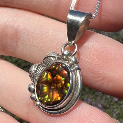 Close-up of vintage fire agate pendant with sterling silver Southwest-inspired design, held in hand under sunlight.