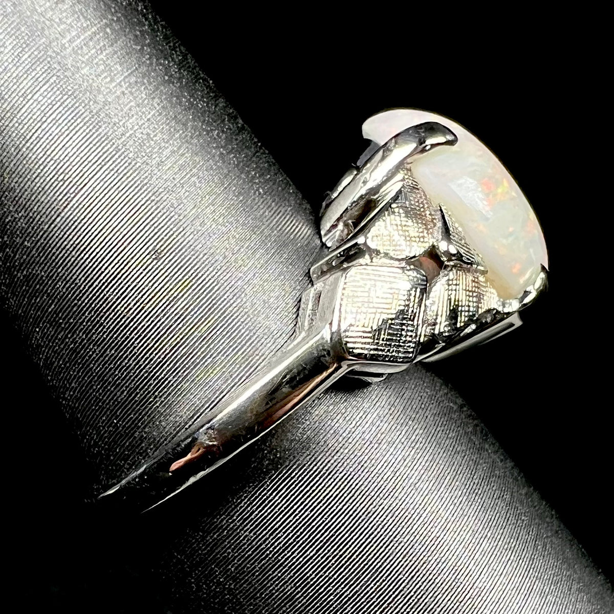 A vintage, textured 14k white gold Australian opal ring on a ring display, shown from the side view, its shank in focus
