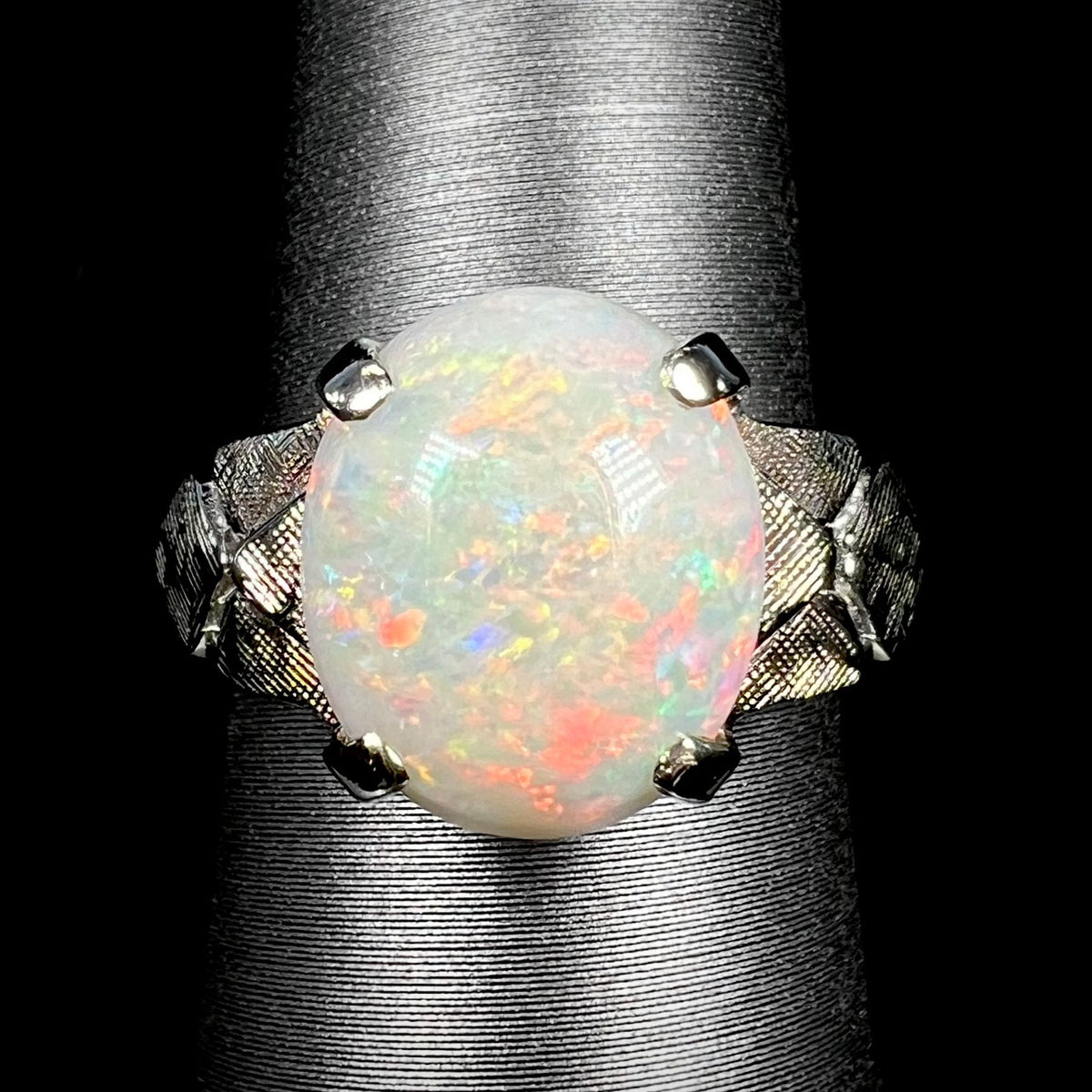 Close-up of a vintage c.1960s era Australian opal solitaire ring with textured 14k white gold shoulders, shown on ring display