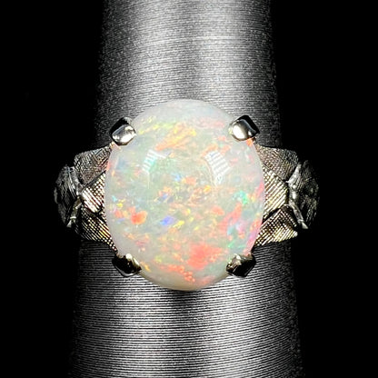 Close-up of a vintage c.1960s era Australian opal solitaire ring with textured 14k white gold shoulders, shown on ring display