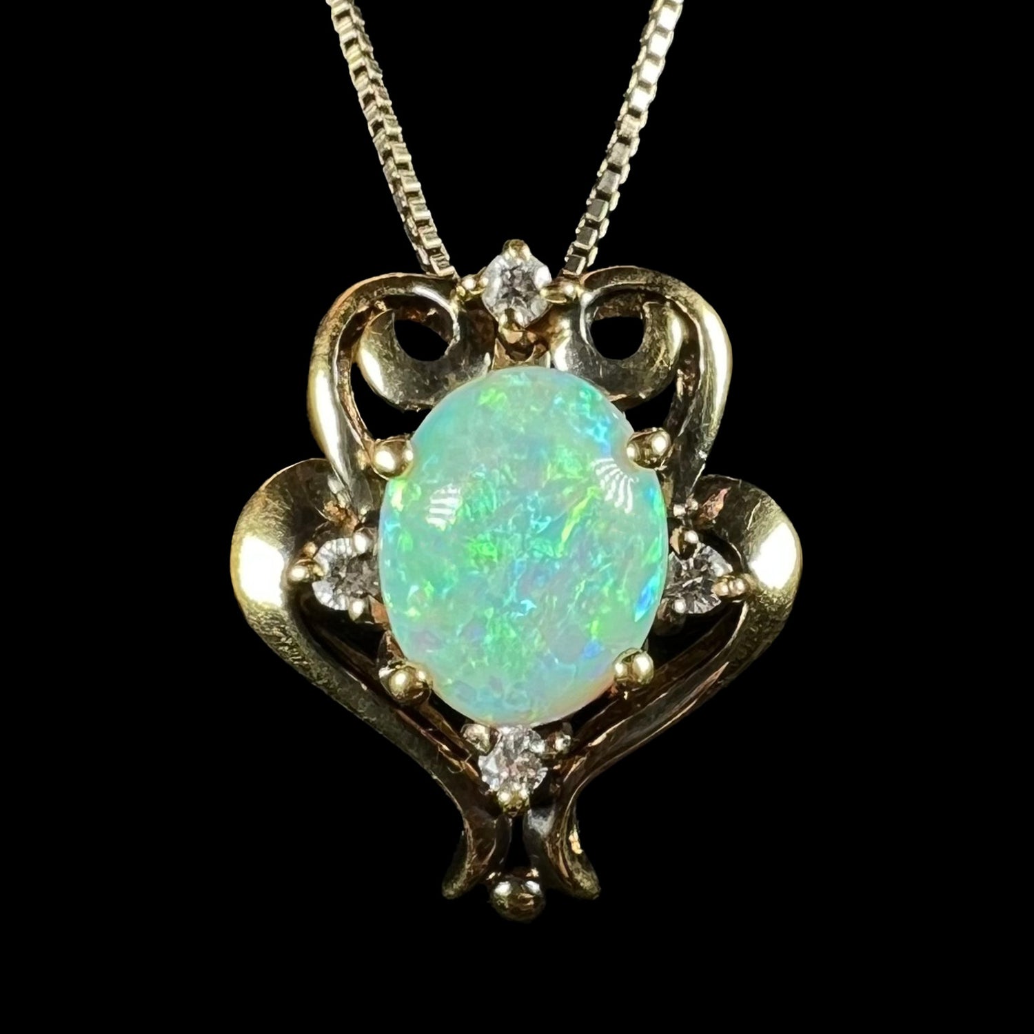 Close-up front view of a women's vintage, Victorian-inspired gold-tone lab-created opal and CZ pendant shown on a silver chain against a black background.