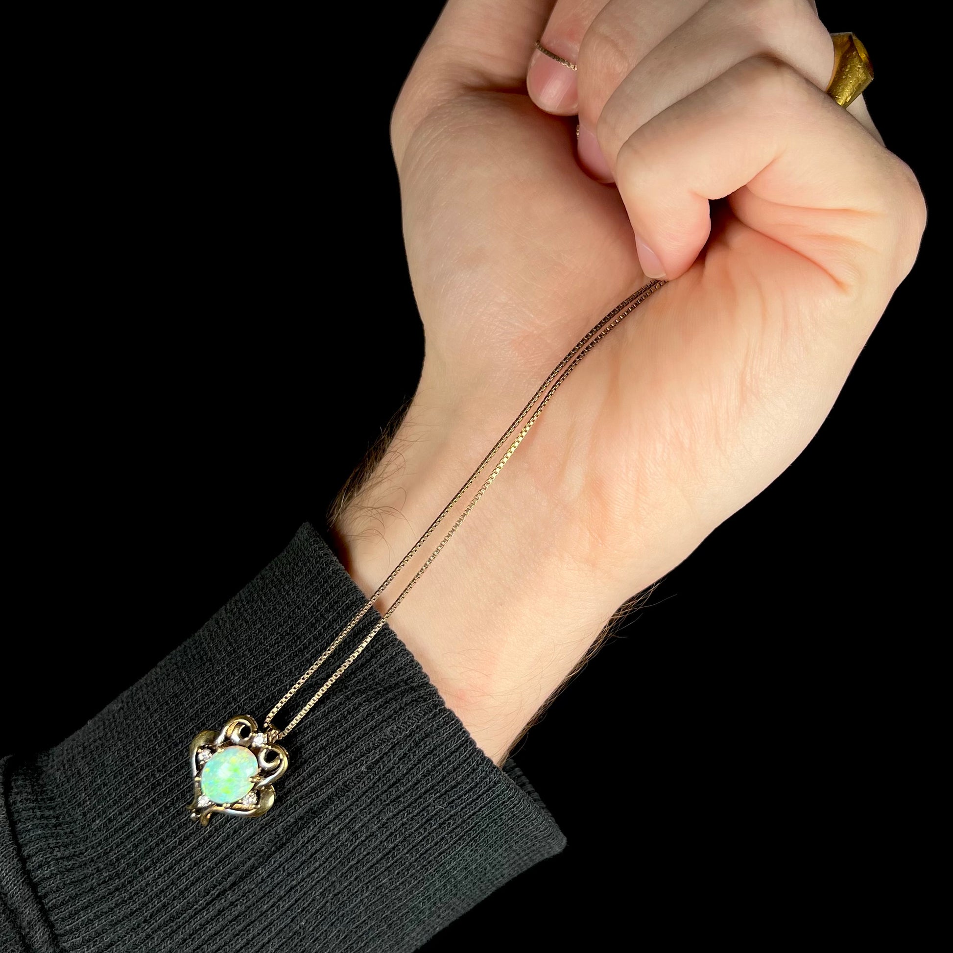 Hand holding a Victorian style opal necklace so that it dangles from its sterling silver chain against the person's wrist.