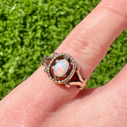 A ladies' Art Nouveau style opal solitaire ring.  The mounting is yellow gold with filigree accents.