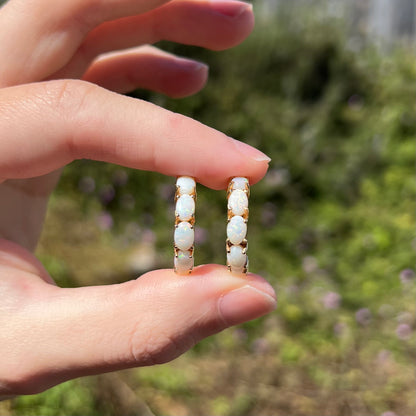 Hand holding pair of vintage gold women's opal hoop earrings between two fingers in sunlight
