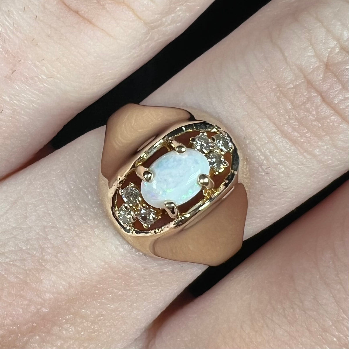 Close-up of vintage 1960s era women's opal and diamond ring in 14k gold, worn on finger under cool LED studio light