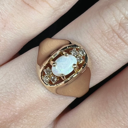 Close-up of vintage 1960s era women's opal and diamond ring in 14k gold, worn on finger under cool LED studio light