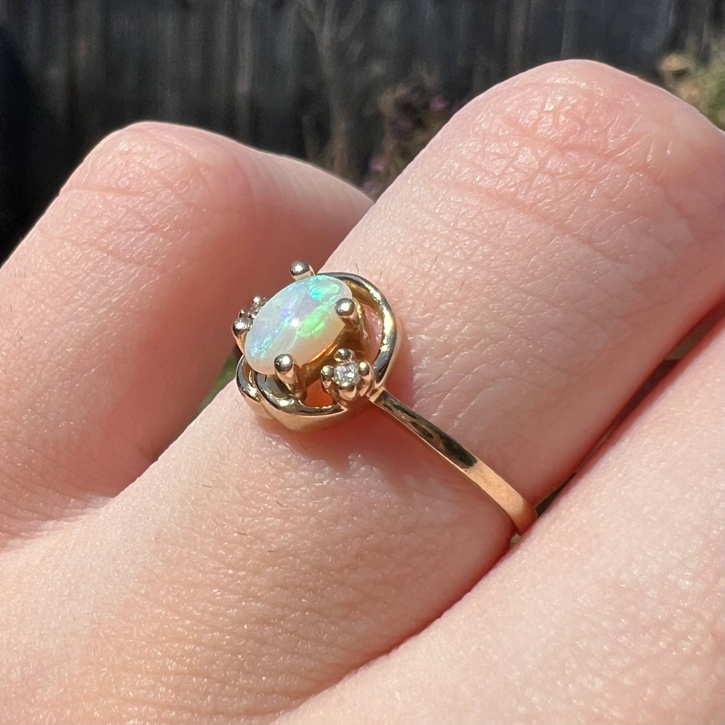 Finger wearing a vintage yellow gold opal and diamond ring, shown from an angle close-up in sunlight.