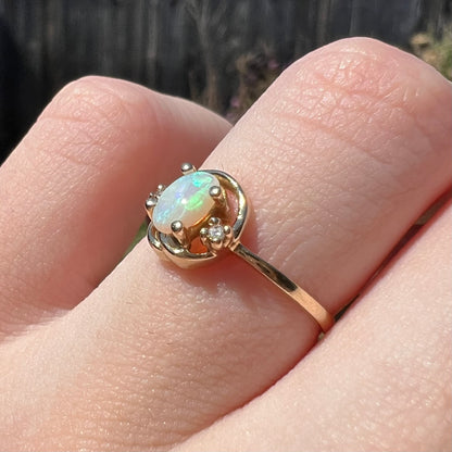 Finger wearing a vintage yellow gold opal and diamond ring, shown from an angle close-up in sunlight.
