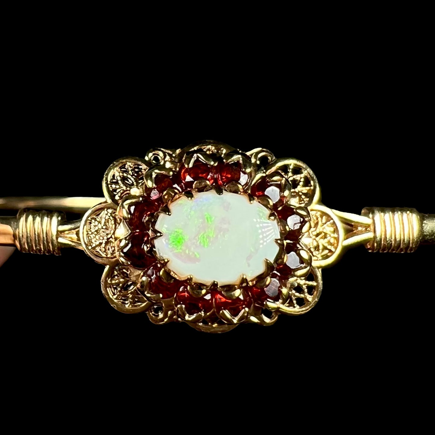 A vintage yellow gold Australian opal and garnet halo bangle bracelet shown close-up against a black background.