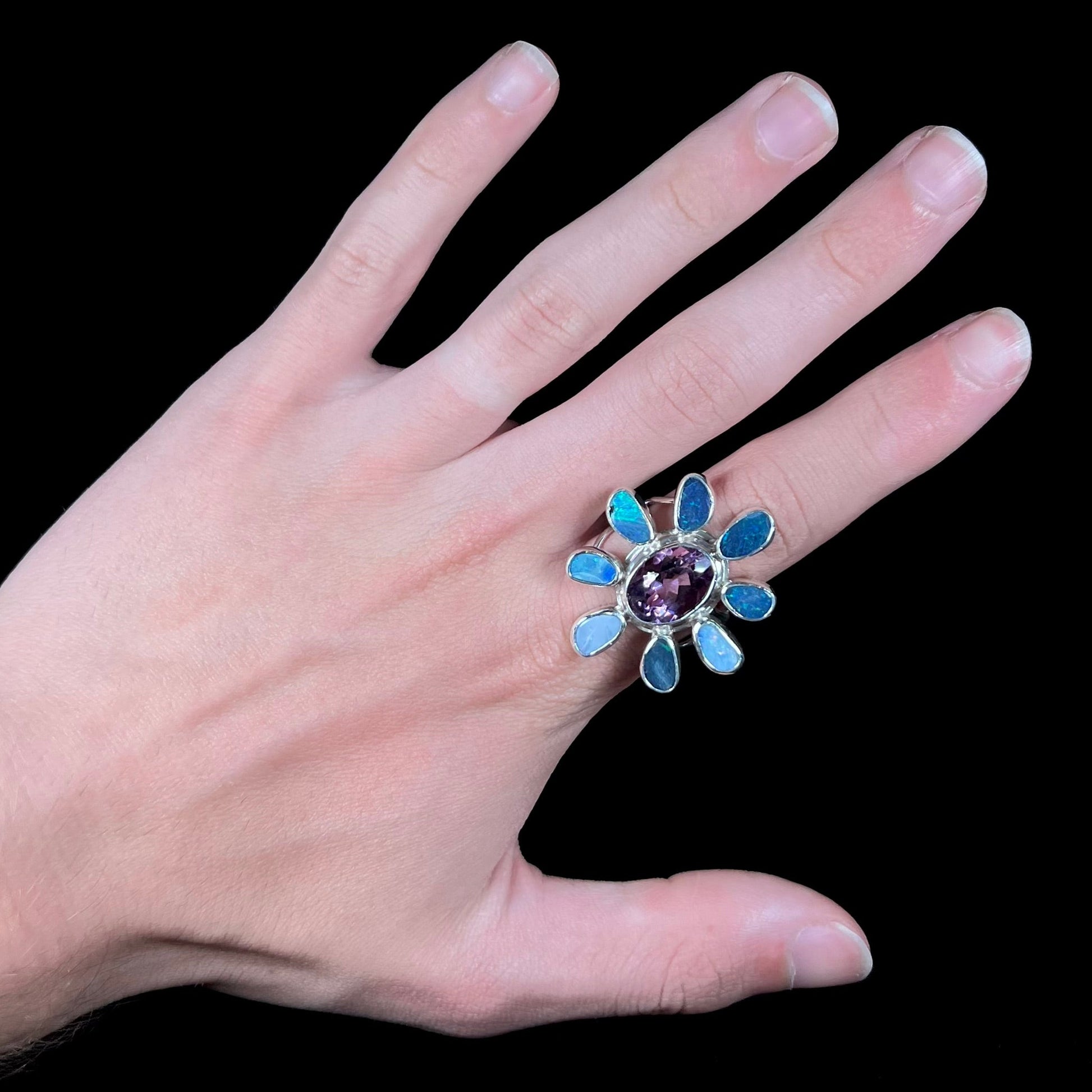 A sterling silver flower shaped ring set with an oval cut amethyst in the center and black opal doublet petals.