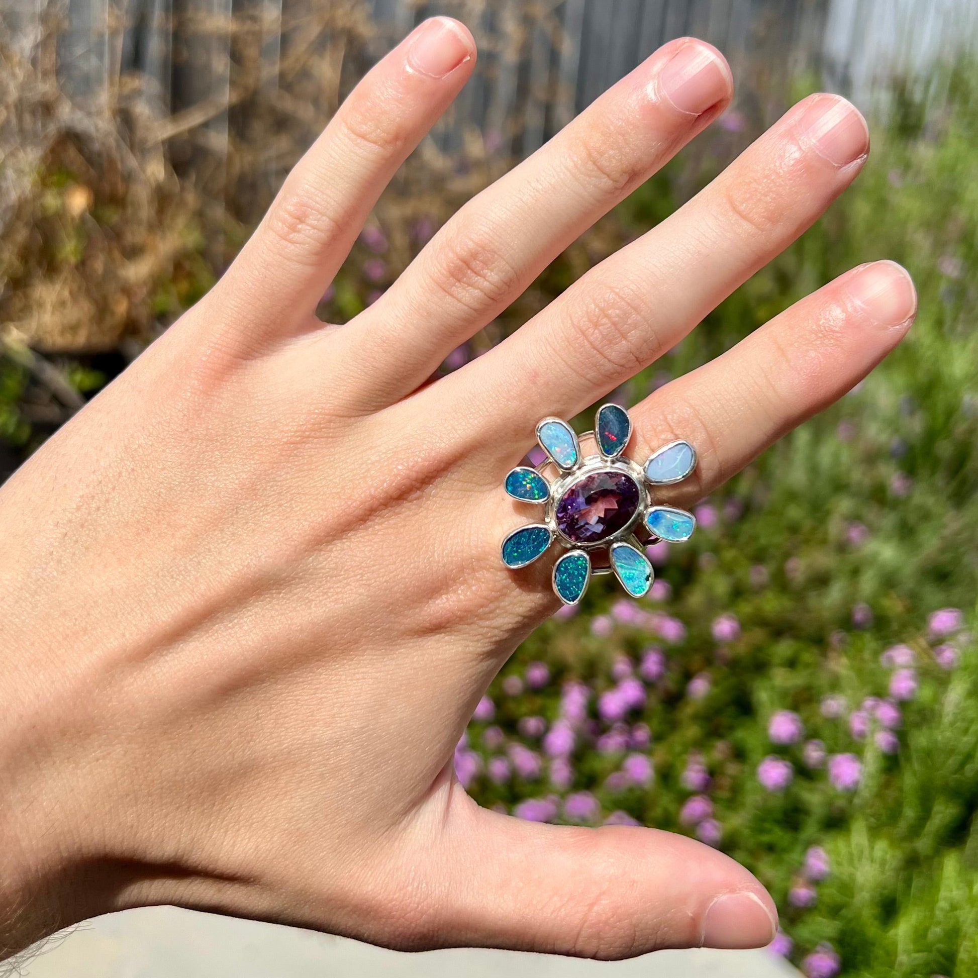 A sterling silver flower shaped ring set with an oval cut amethyst in the center and black opal doublet petals.