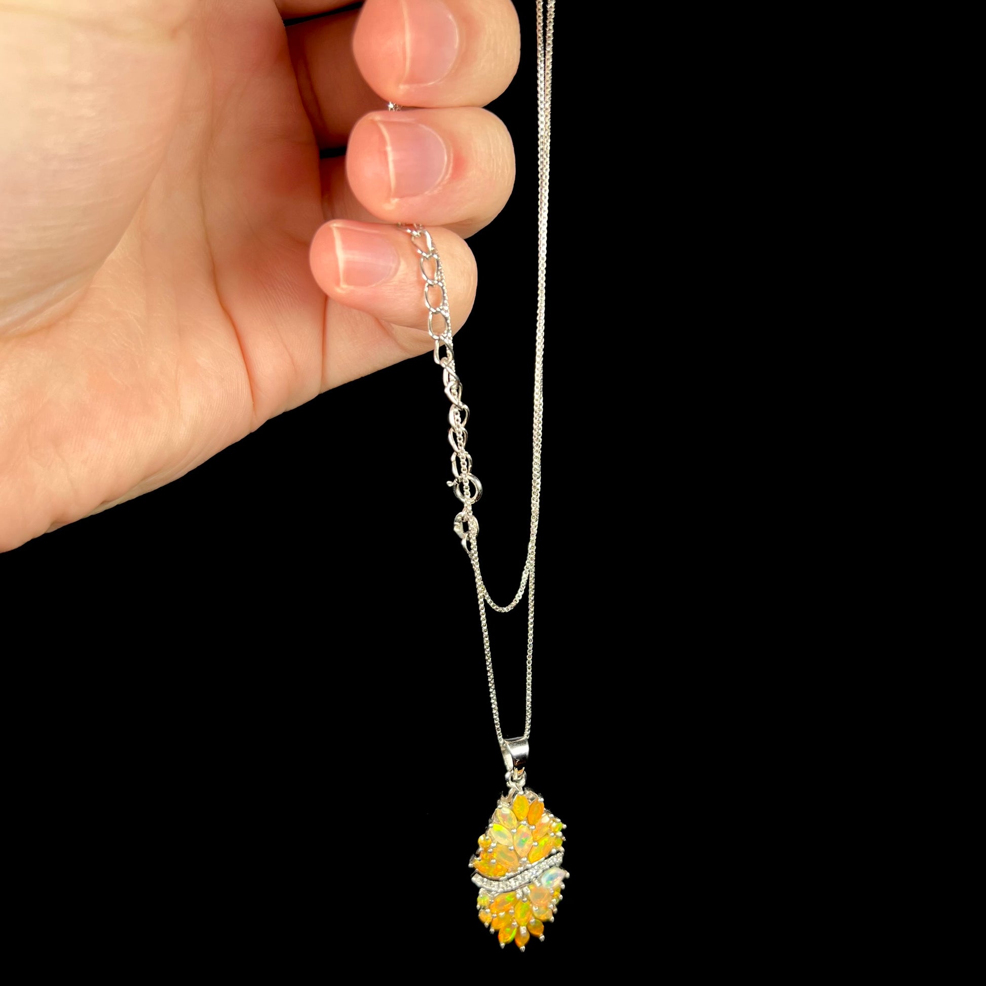 Hand dangling a warm orange Ethiopian fire opal necklace from its sterling silver chain.