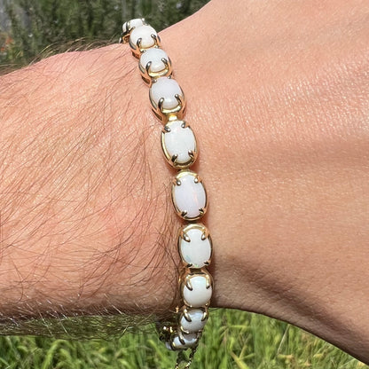 Close-up of a white Australian opal tennis bracelet in 10k yellow gold, worn around a wrist in natural sunlight.