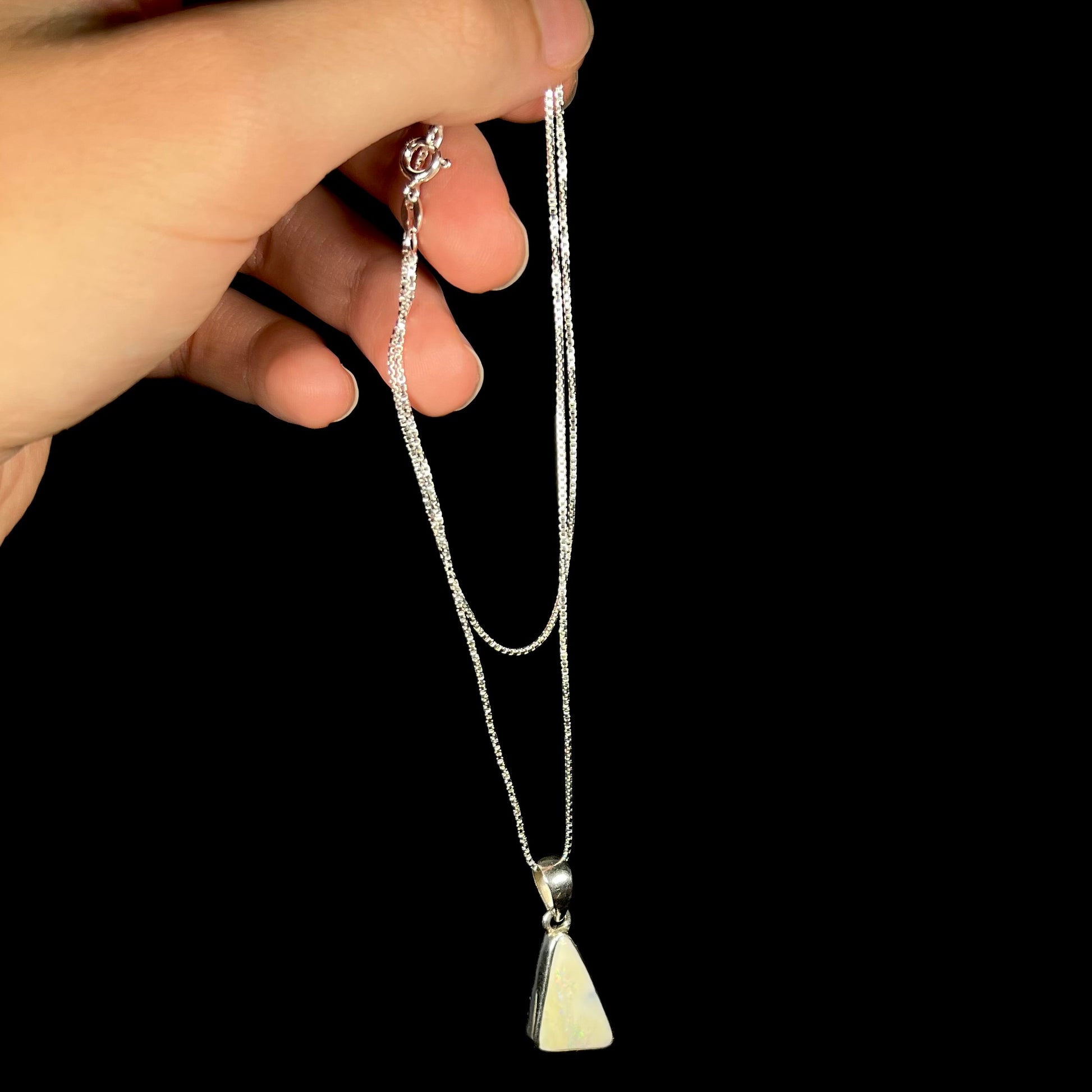 A white Australian boulder opal necklace in .950 silver, shown dangled by a hand from its chain.