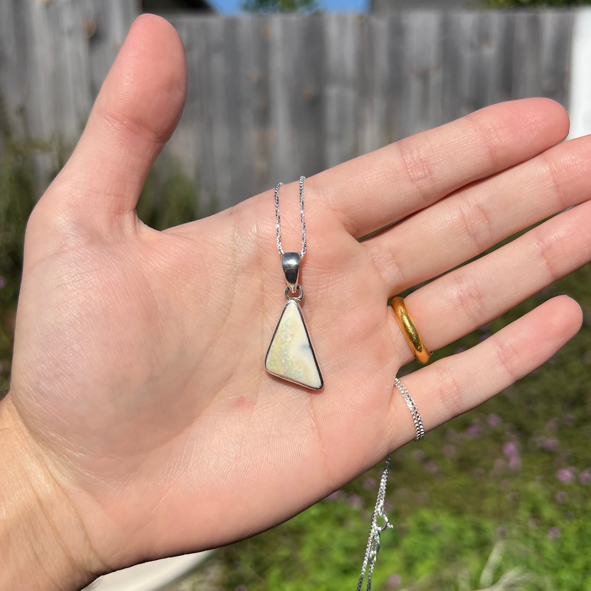 A white Australian boulder opal necklace in .950 silver, shown in a hand in outdoor sunlight.