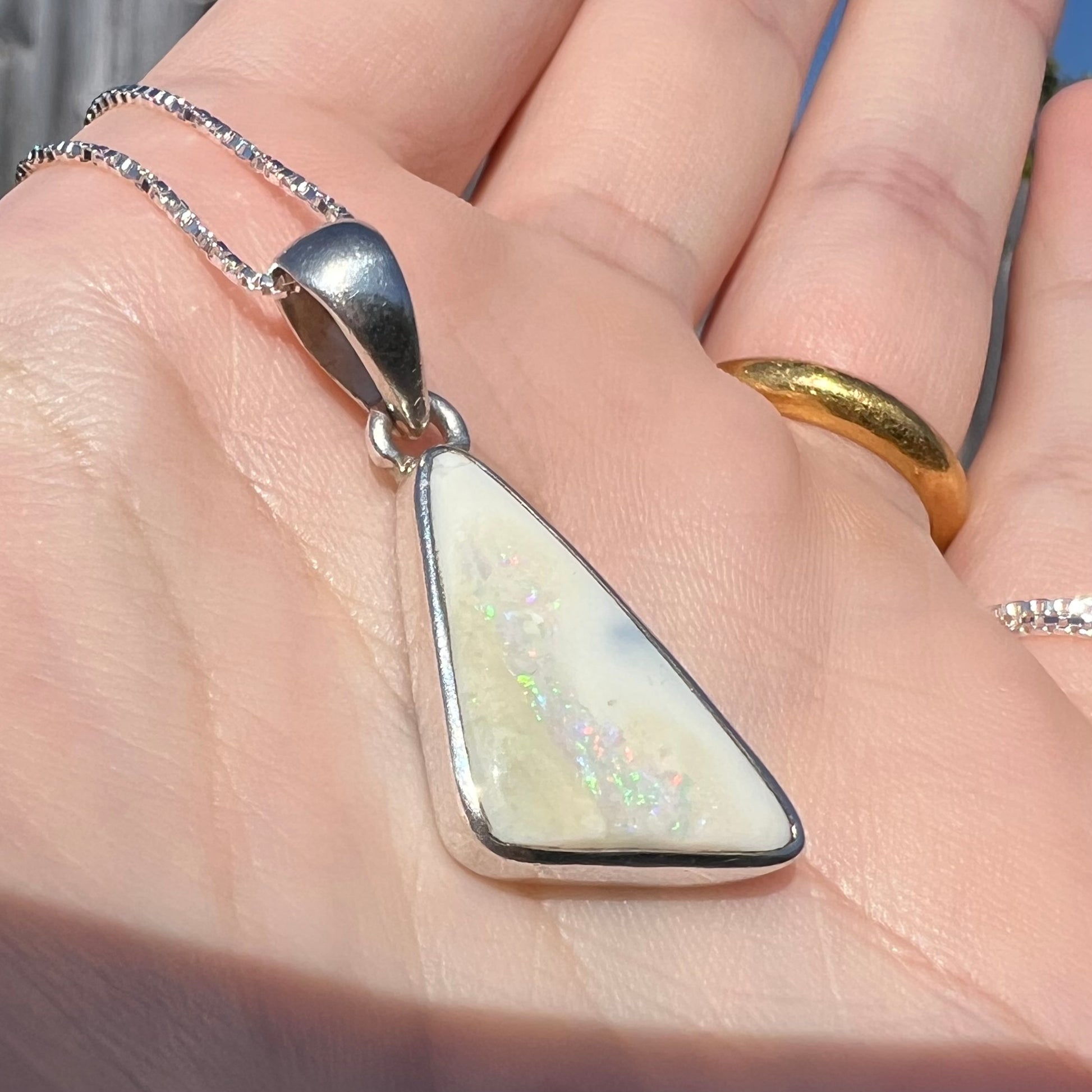 A white Australian boulder opal necklace in .950 silver, shown at a close-up angle in a hand in sunlight.