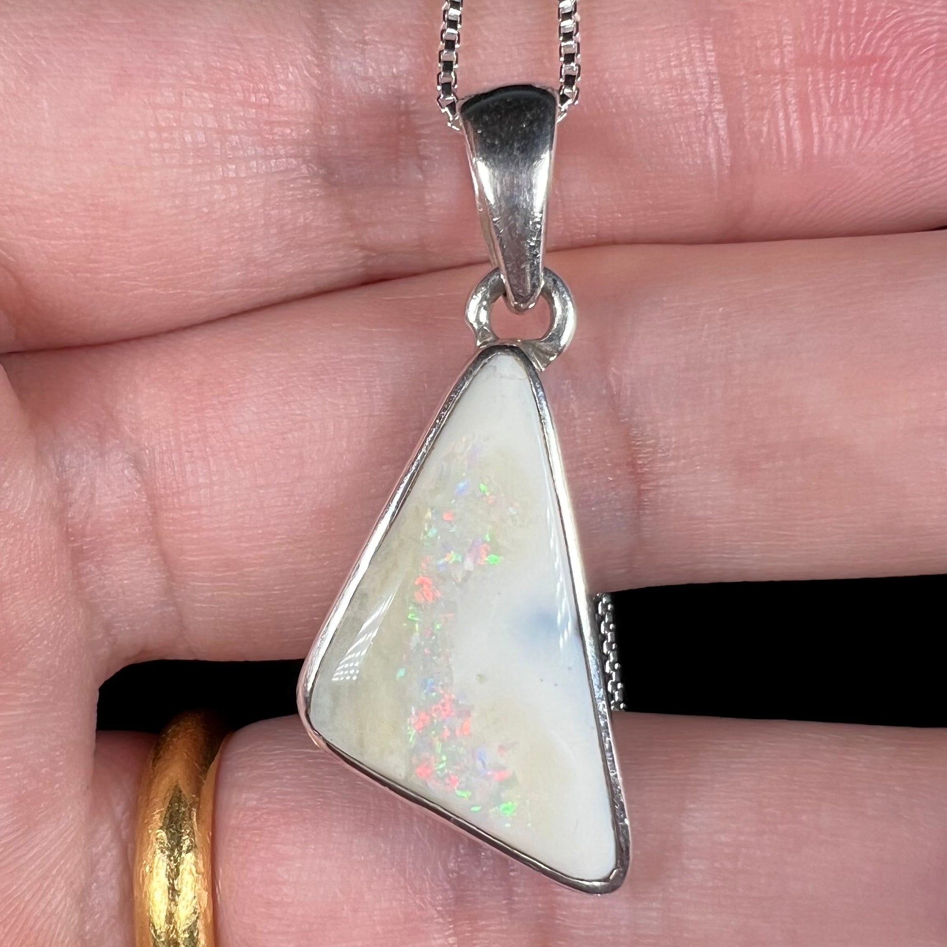A white Australian boulder opal necklace in .950 silver, shown close-up in a hand.