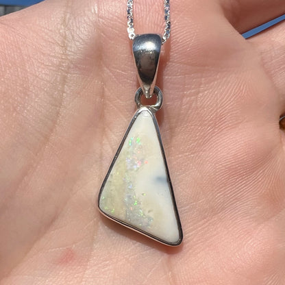 A white Australian boulder opal necklace in .950 silver, shown close-up in natural sunlight, held in a hand.