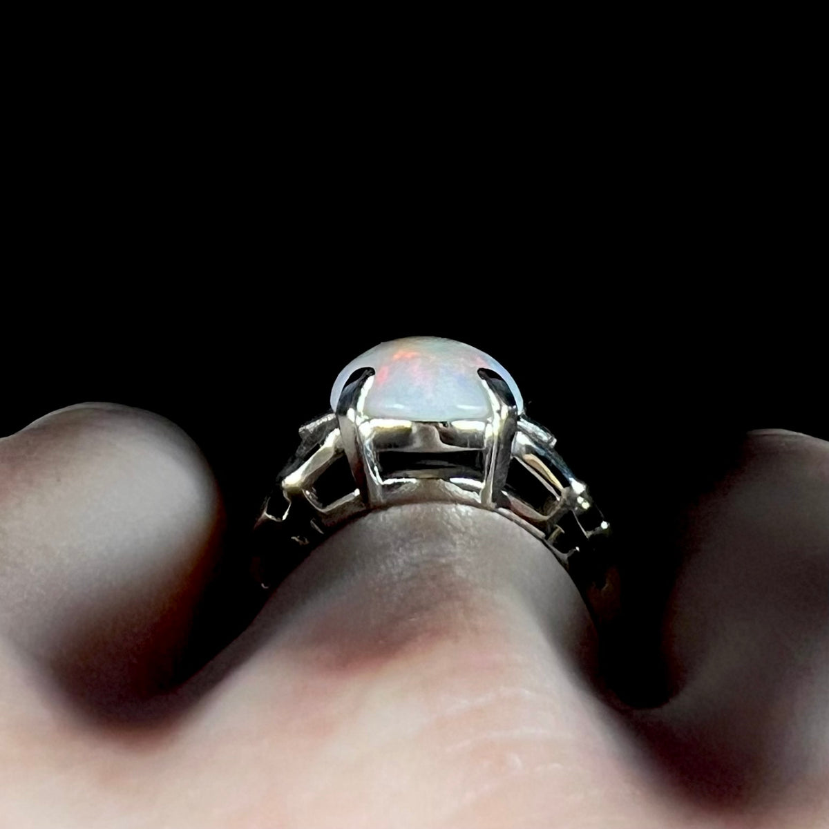 Side gallery profile view of a white gold Australian opal ring, worn on a hand; the ring's prong-set basket and the opal's dome are in focus