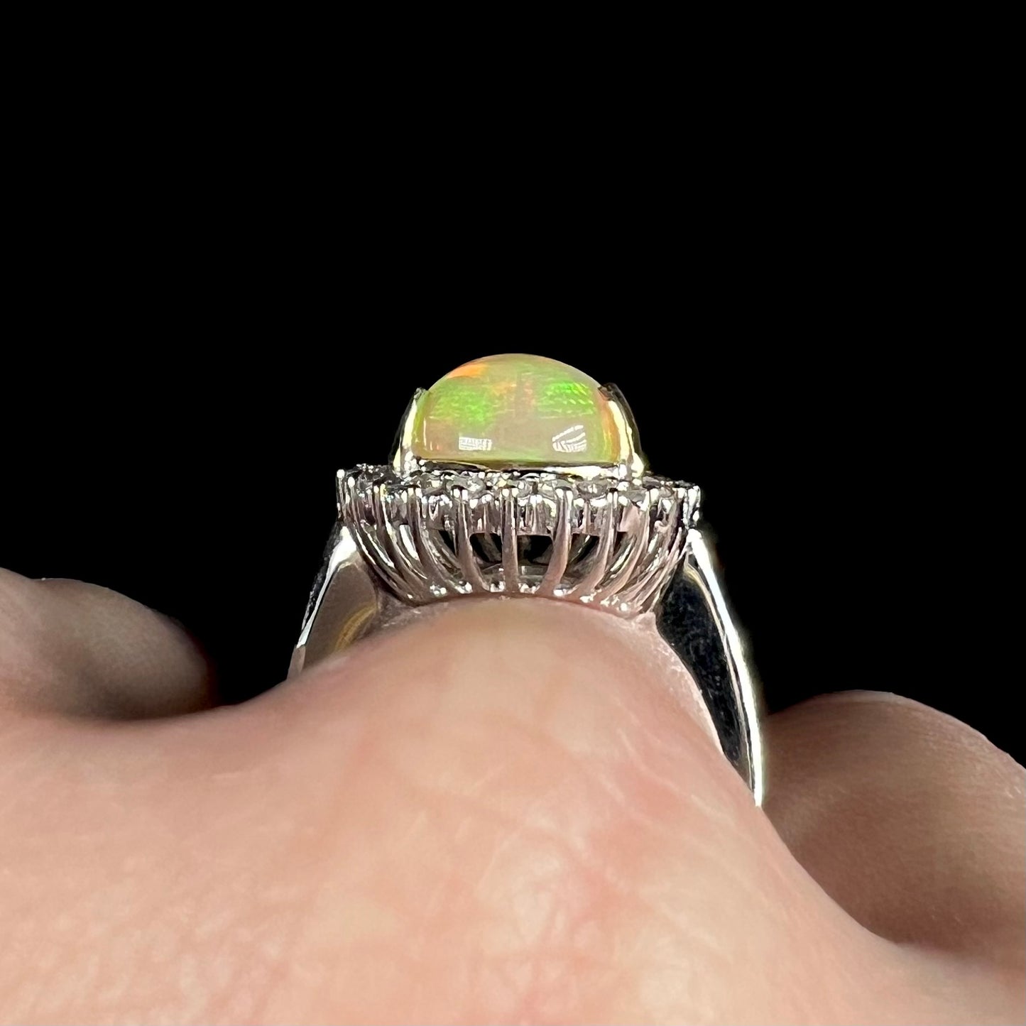 Side gallery basket view of a white gold fire opal ring worn on a hand.