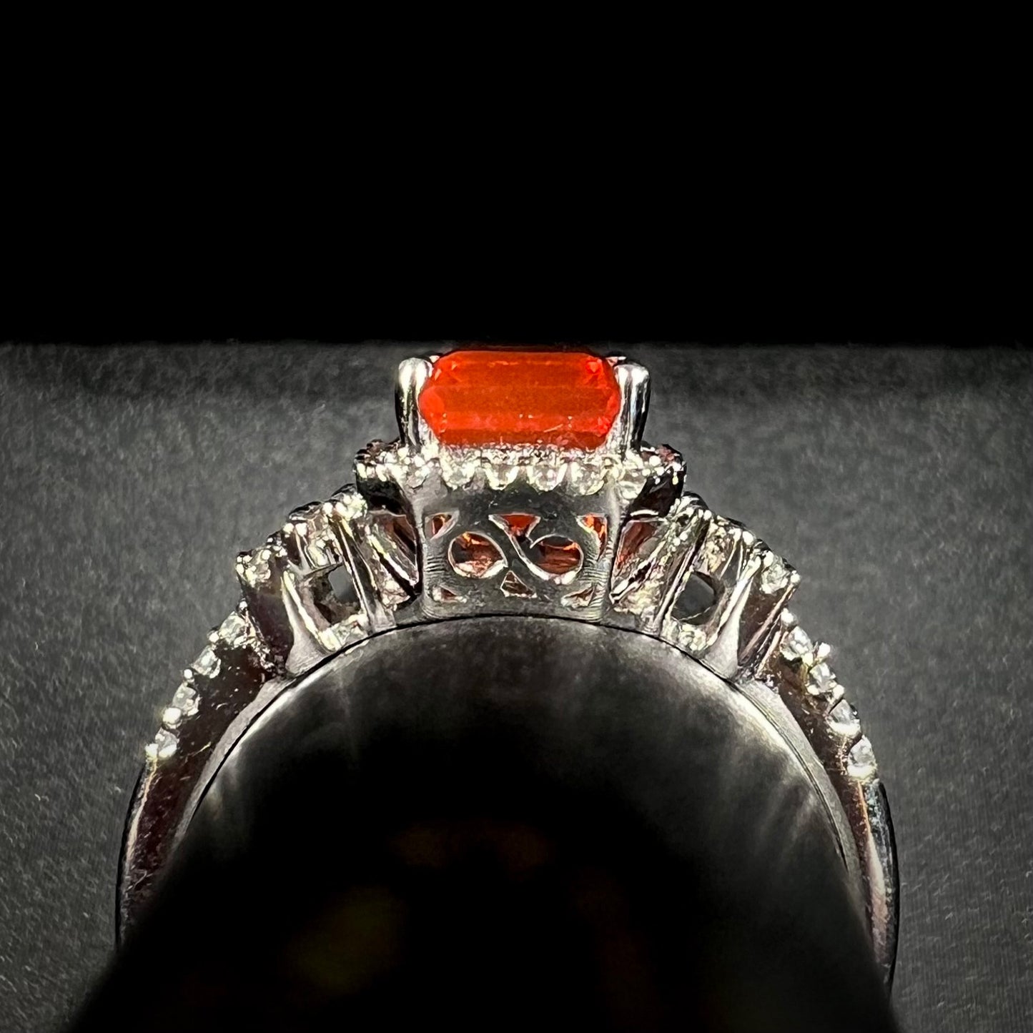 Side gallery view of white gold fire opal ring shown on a ring display.  Cast filigree is seen on the ring's basket.