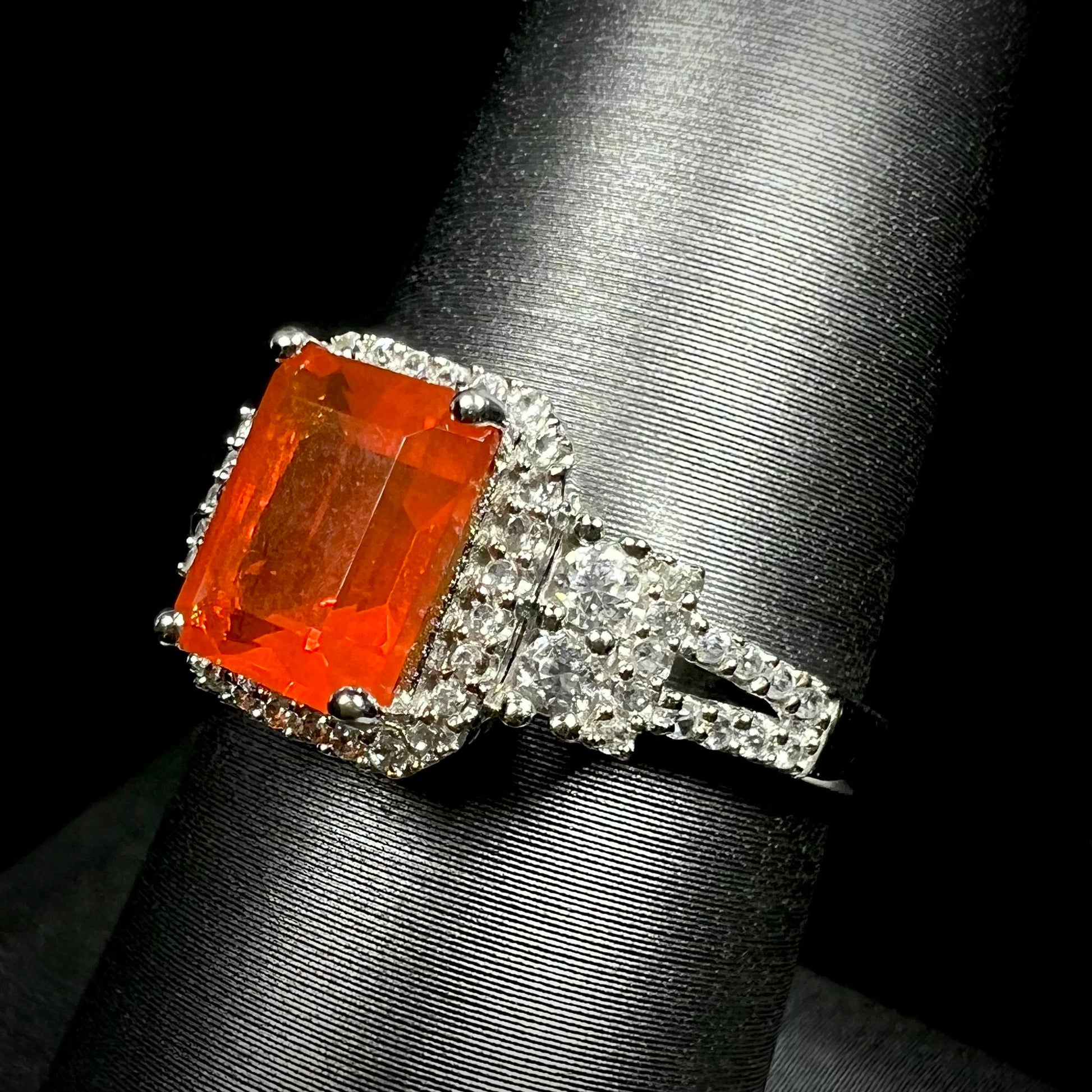 Angled macro view of a fire opal and white zircon halo ring in white gold, shown on a ring display against a black background.