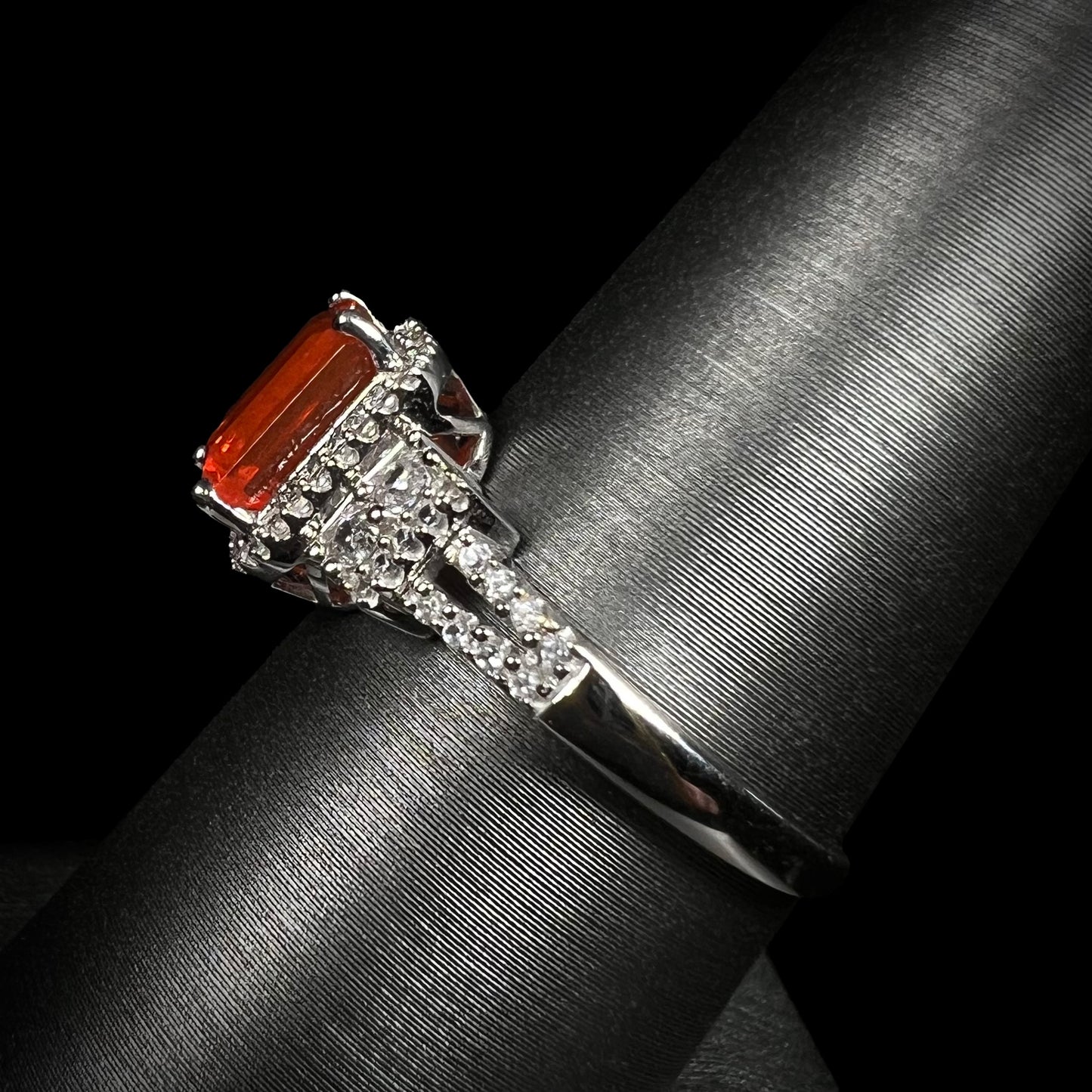 Side view of a white gold fire opal and natural white zircon-accented ring shown on a ring display against a black background.