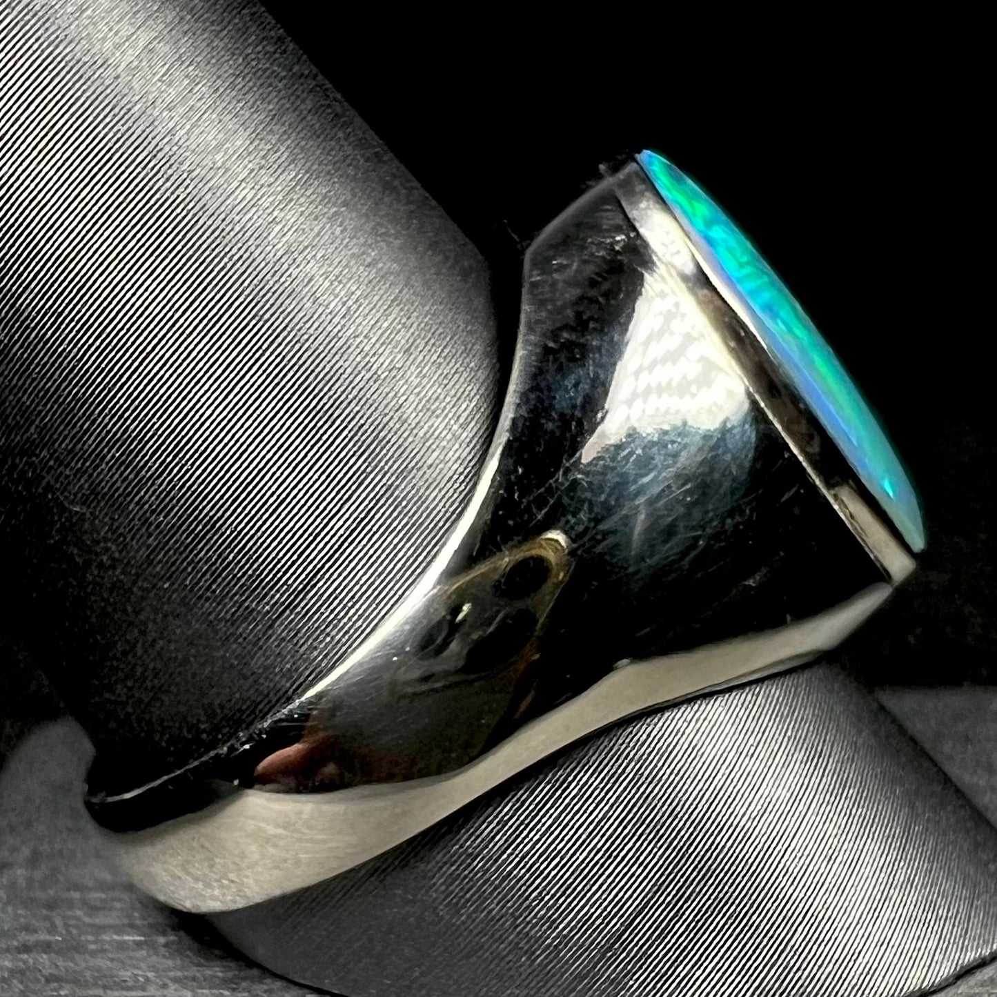 Side view of solid white gold Australian opal men's ring on ring display, focused on ring's heavy shank